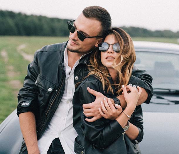 A couple in sunglasses embracing near luxury car in countryside