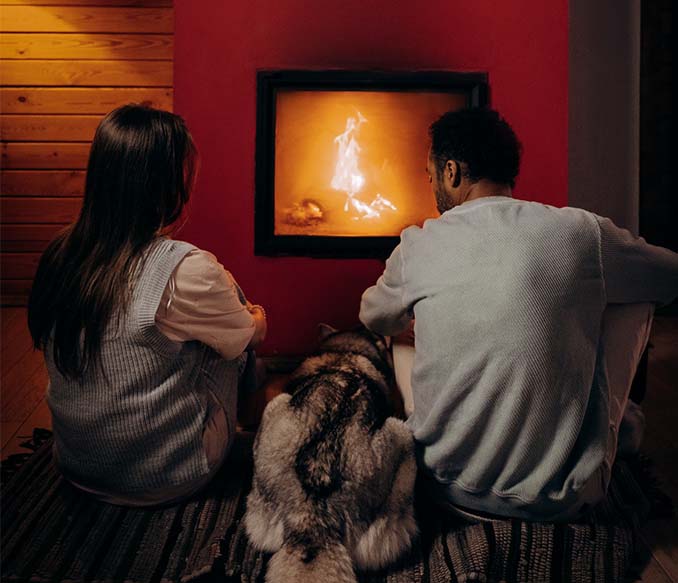 A couple sitting near fireplace with their dog