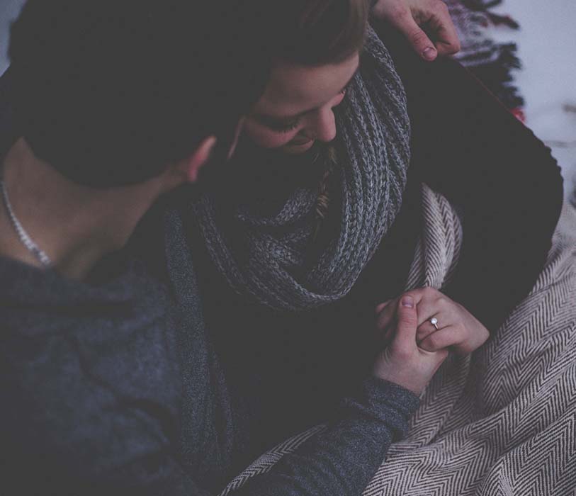 A couple with a grey blanket holding each other's hands