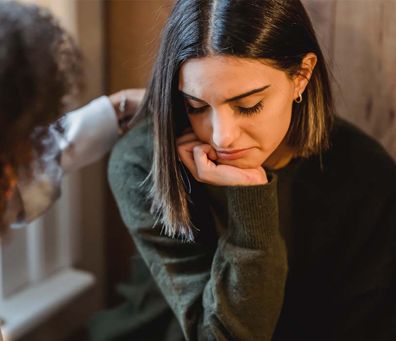 A crop woman tapping shoulder of frustrated female friend