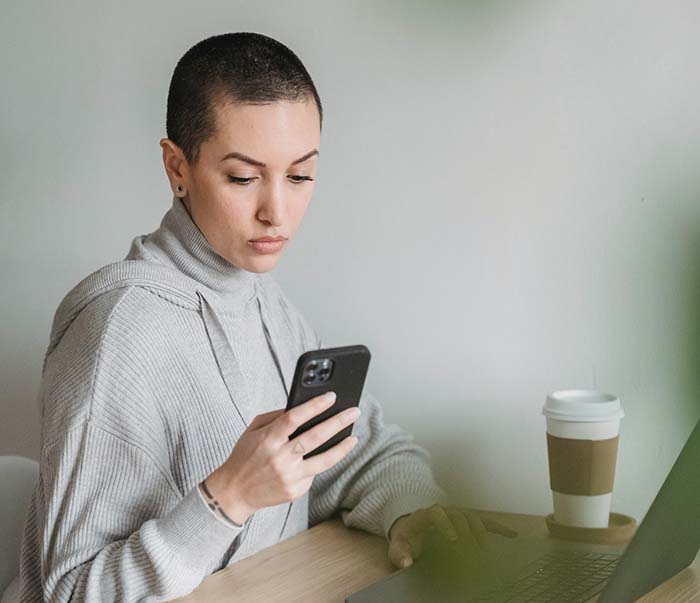 A focused woman using smartphone and working on laptop