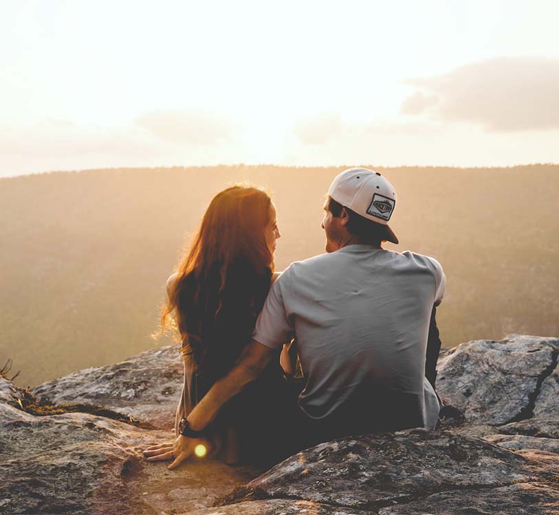 A man and a woman sitting on rock during daytime