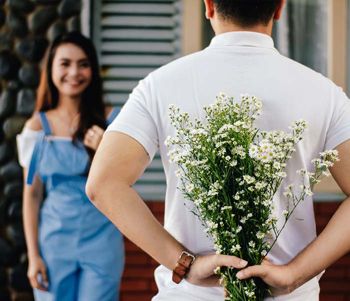 A man holding baby's breath flower in front of woman standing near marble wall