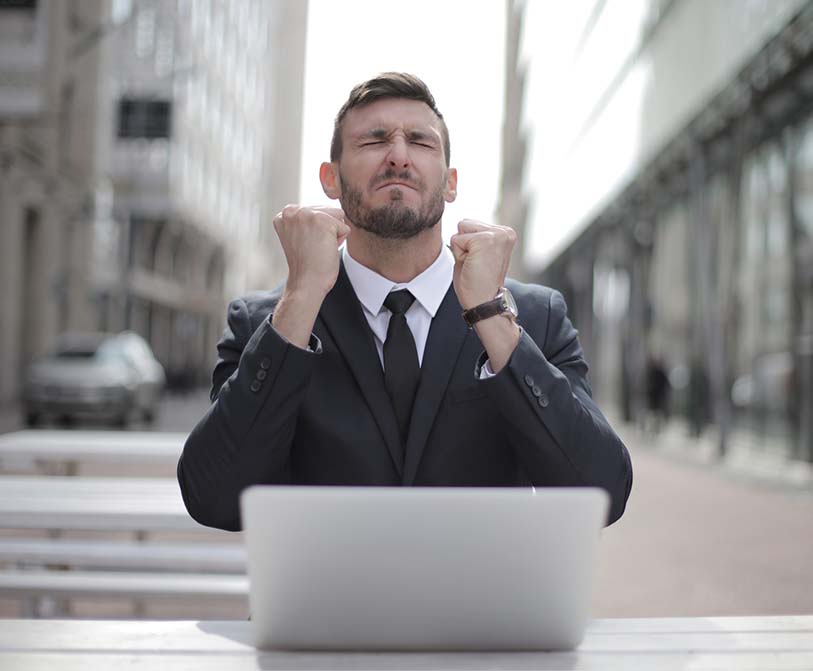 A man in a black suit sitting on a chair behind buildings