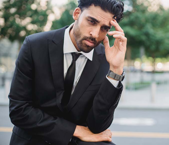 A man in a black suit with his hand on his head