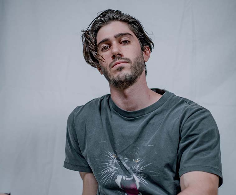 A man in a grey neck t-shirt sitting on bed