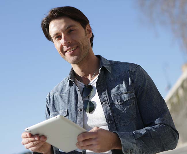 A man in ablue denim shirt holding white tablet