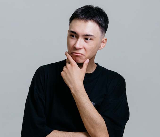 A man in black crew neck shirt thinking with his hand on his chin