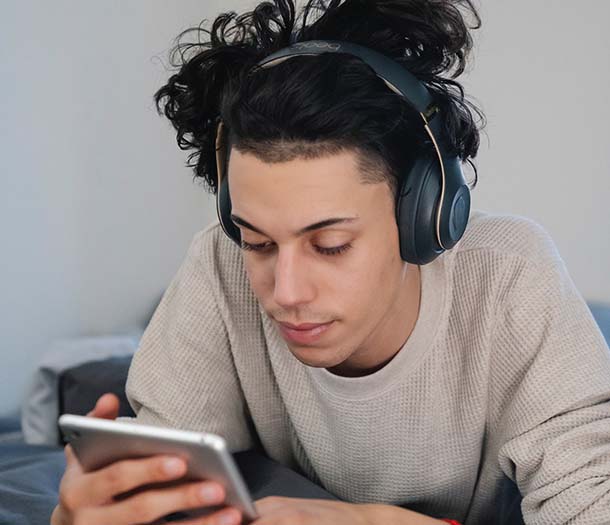 A man in headphones surfing internet on smartphone on bed