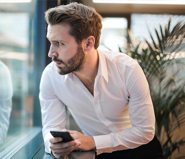 A man leaning on glass window holding a smartphone