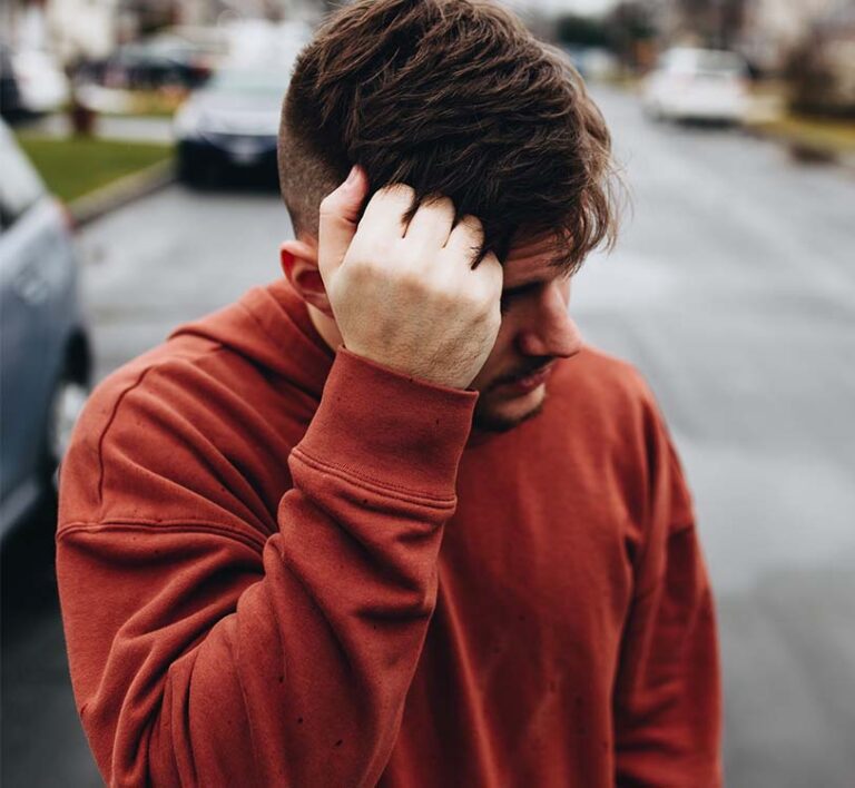 A man walking on road with left hand on head