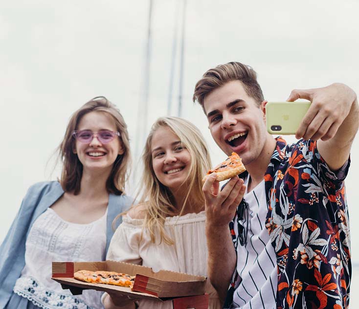 A man with two women taking a selfie while eating pizza