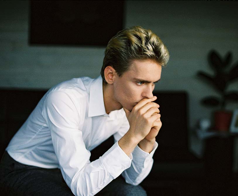 A nervous young man leaning on his hand and thinking in a room