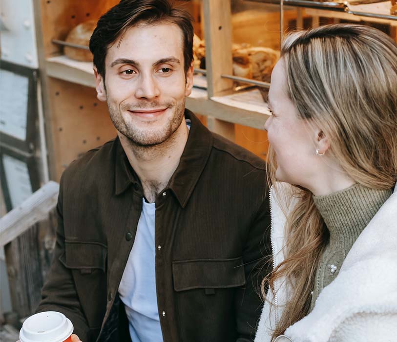 A positive young man enjoying hot beverages with girlfriend while sitting near cafeteria