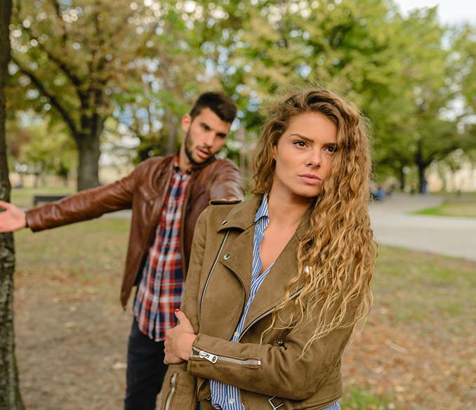 A woman and a man wearing brown jackets standing near tree