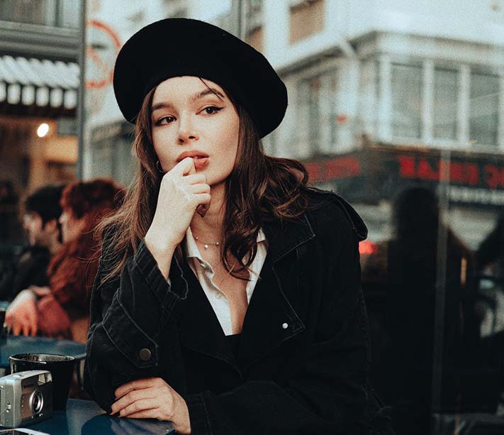 A woman sitting and posing in black coat and hat