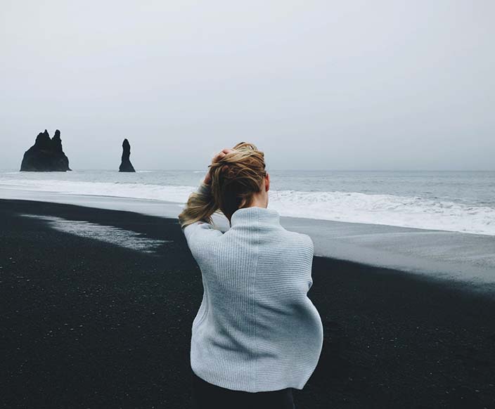 A woman wearing sweater standing in front of beach