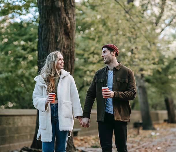 A young couple holding hands and drinking coffee while walking in park
