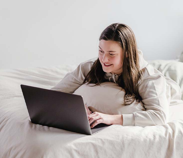 A young lady relaxing on bed and watching movie on laptop