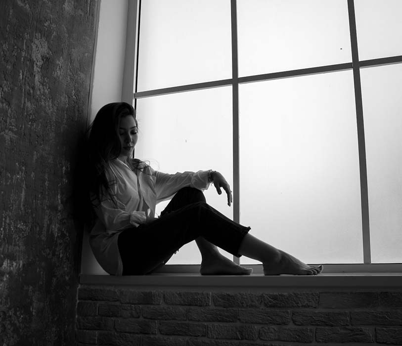 A young unhappy woman sitting in solitude near window
