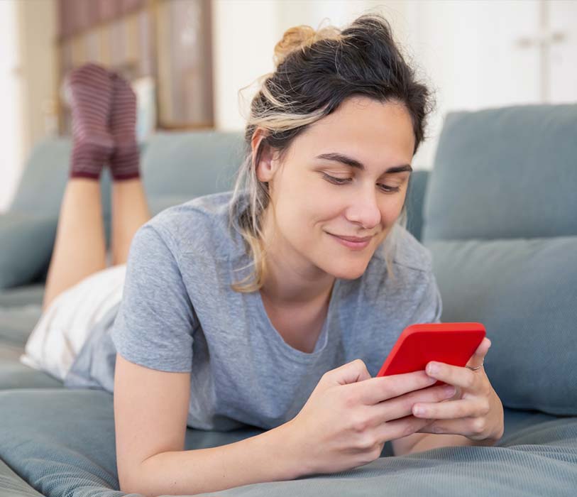 Close up shot of a woman lying on sofa while using her cellphone