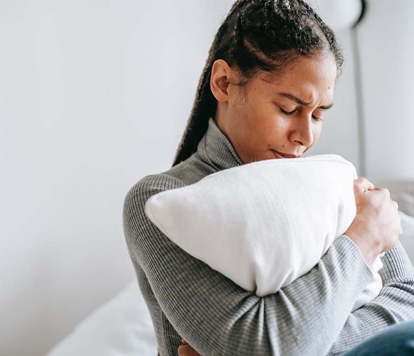 Ethnic sad woman embracing pillow in solitude