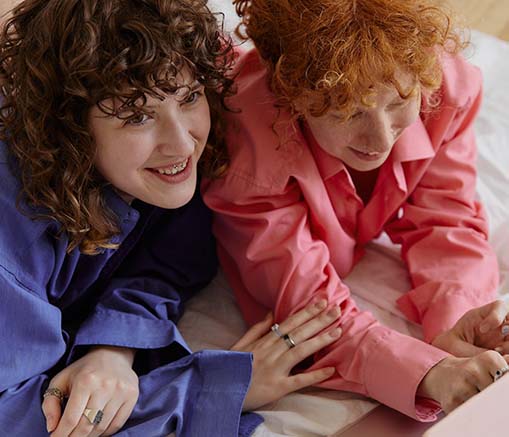 Two women in pink long sleeves lying on floor with white textile