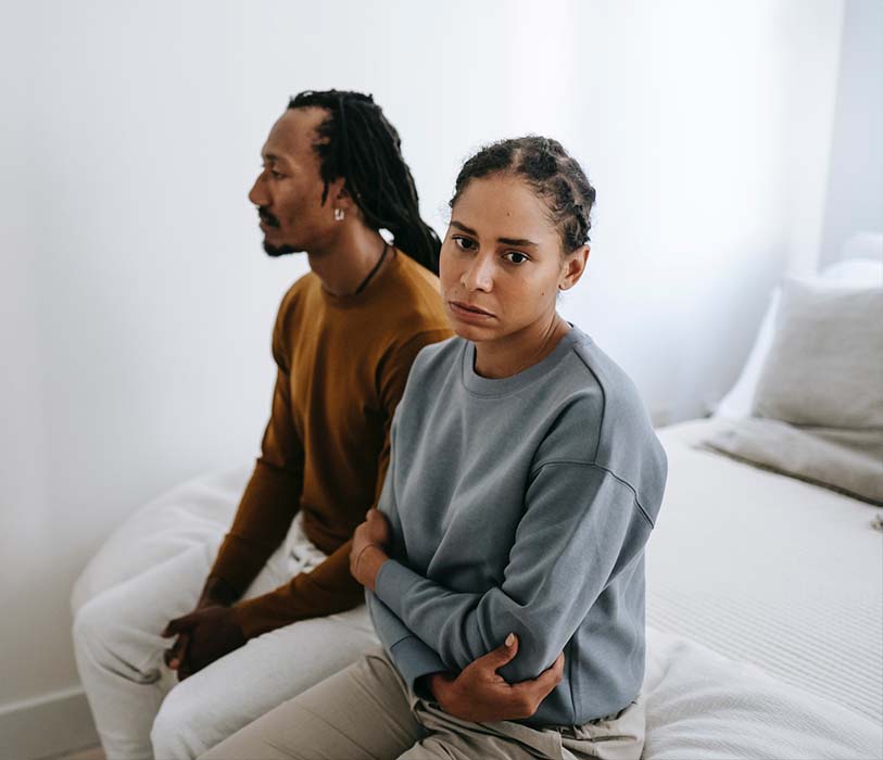 Unhappy black couple sitting on bed together