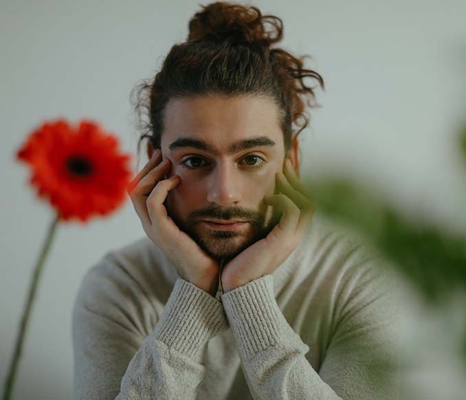 a bearded man in beige sweater with his hands on his face