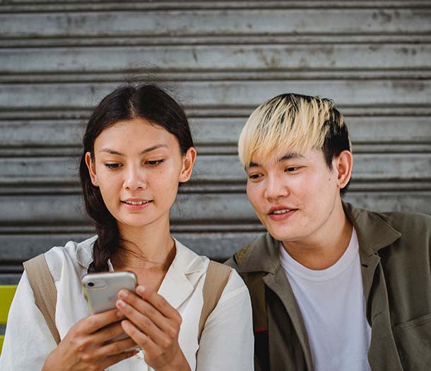 cheerful asian couple browsing smartphone on street bench