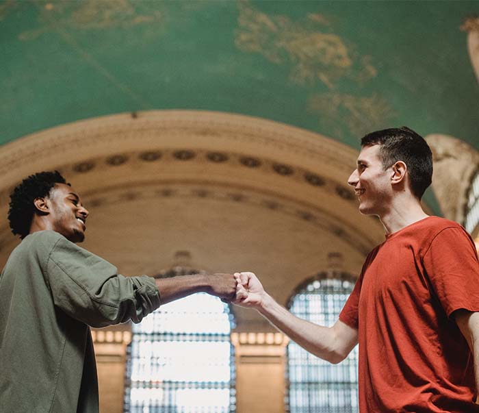 cheerful young multiracial male friends bumping fists in old building