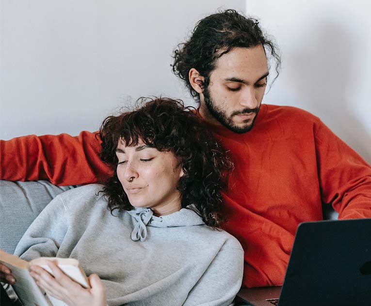 ethnic couple with laptop and book resting on sofa