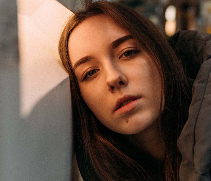 thoughtful young female leaning on wall and looking at camera