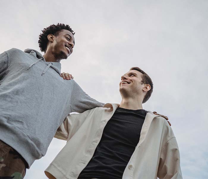 two male friends side hugging against cloudy sky