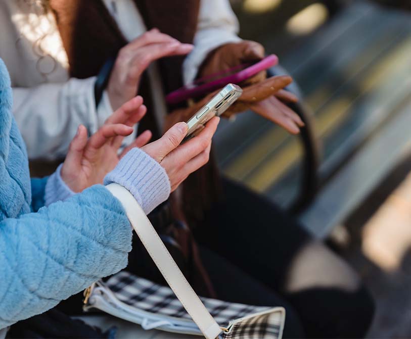 women touching screens of smartphone in a park
