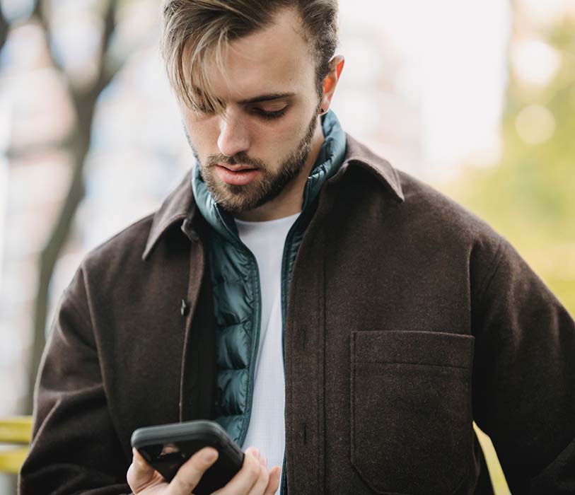 young hipster looking at smartphone screen in park
